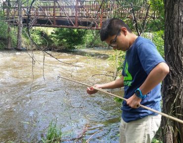 Groundwork Denver Blue Team member Fernando Chavez collecting a water sample from the Bear Creek in Sheridan